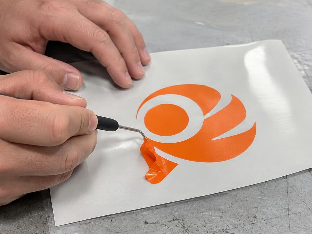 Handen wieden overtollige oranje flexfolie van een uitgesneden logo